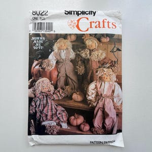 May include: Simplicity Crafts pattern 8022 showing four scarecrow dolls in different outfits, posed with pumpkins. The text "MOMMA MADE ME DO IT!" is visible. The pattern is one size.