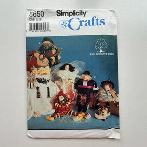 May include: Simplicity Crafts sewing pattern for making dolls. The pattern shows several doll designs, including a clown, a bride, and a gentleman. The cover has the text "Simplicity Crafts" and "The Buckeye Tree".