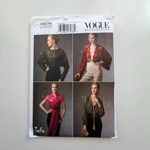 May include: Vogue Accessories sewing pattern envelope featuring four different bolero jacket designs. The envelope is white with the Vogue logo and the number V9276. The designs include a black lace bolero, a red lace bolero, a pink wrap, and a gold patterned jacket.