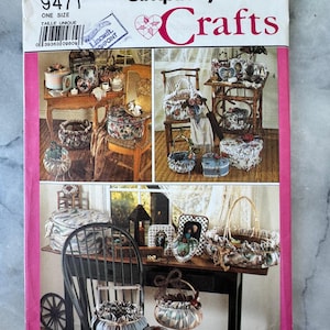Könnte beinhalten: Ein Vintage-Simplicity Crafts-Schnittmuster mit verschiedenen Stoffhandwerksprojekten. Das Cover zeigt Bilder von dekorativen Körben, Schachteln und anderen handgefertigten Artikeln. Die Modellnummer ist 9471, und das Cover hat einen rosa Rand.