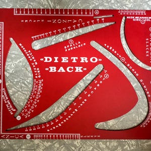 Könnte beinhalten: Ein rotes Schneider-Messwerkzeug mit weißen Markierungen und Text. Das Werkzeug verfügt über gebogene und gerade Kanten mit Messungen in Zentimetern. Der Text enthält "DIETRO BACK", "MANICA SLEEVE" und "CALZONI SLACKS".