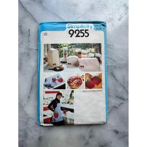Op de afbeelding: Een vintage Simplicity naaipatroon, nummer 9255, met afbeeldingen van keukenaccessoires met aardbeienapplicaties. Het patroon bevat instructies voor het maken van items zoals een broodroosterhoes, broodwarmer en schort. De rand is blauw en wit.