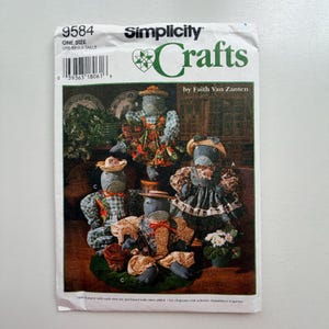 May include: Simplicity Crafts pattern 9584, showcasing fabric doll designs. The cover displays dolls with hats and dresses, highlighting various fabrics and styles. The pattern is by Faith Van Zanten.