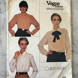 Op de afbeelding: Vintage Vogue Patterns naaipatroon met drie blouse-ontwerpen. De omslag bevat de tekst "Vogue Patterns AMERICAN DESIGNER" en "Calvin Klein" samen met patroonnummer 1025. De blouses zijn in tinten beige en crème.