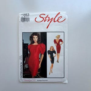 May include: A vintage sewing pattern labelled "Style" from 1983. The pattern shows dress designs with puffed sleeves. The cover includes the text "SIZE A (6-16)" and "PATTERN/PATRON A (32-42)".