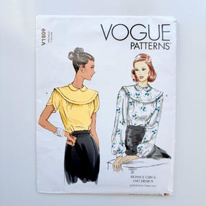May include: A Vogue Patterns sewing pattern envelope V1809 featuring two illustrations of blouses with Peter Pan collars. One blouse is solid yellow with short sleeves, and the other is a long-sleeved white blouse with a blue and green floral print.