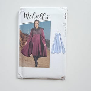 Op de afbeelding: Een McCall's M7854 naaipatroon-envelop met een bordeauxrode jurk met een donker getextureerd lijfje en wijde mouwen, naast een lijntekening van een lichtblauwe jurk. De tekst bevat McCall's, M7854 en de maat A5 (6-8-10-12-14).