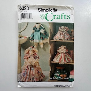 Pode incluir: Padrão de costura Simplicity Crafts com designs de bonecas. O padrão inclui instruções para criar bonecas com vários vestidos e acessórios. A capa exibe várias bonecas acabadas, mostrando os diferentes estilos e tecidos usados nos designs.
