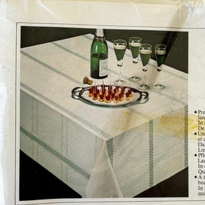 May include: A white tablecloth with a green striped pattern, set for a celebration. A bottle of champagne, glasses, and a tray of appetizers are arranged on the table. The scene evokes a festive atmosphere.