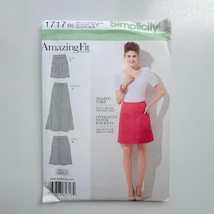 May include: A Simplicity 1717 sewing pattern envelope for the Amazing Fit collection. The front displays a model wearing a pink skirt with oversized patch pockets and a shaped yoke that sits 1 inch below the natural waist, alongside technical line drawings.