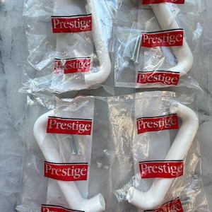 Peut inclure: Quatre poignées de placard blanches dans un emballage plastique transparent avec des étiquettes rouges et blanches "Prestige". Chaque poignée est incurvée et tubulaire, avec une vis.