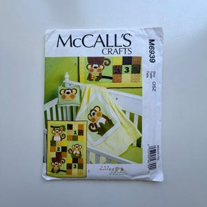 Op de afbeelding: McCall's Crafts naaipatroon voor een babykamer set met apenontwerpen. Het patroon bevat instructies voor een quilt, kussen en andere babykamerartikelen. De ontwerpen bevatten bruine, groene en gele kleuren.