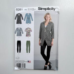 Op de afbeelding: Simplicity naaipatroon 8261 voor maten 14-22. De envelop bevat illustraties van vijf verschillende wikkelshirts en twee broeken. Een foto toont een model in een zwart-wit patroon wikkelshirt met een zwarte legging.