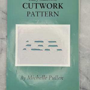 Könnte beinhalten: Ein türkisfarbenes Buch mit dem Titel "Easy Machine Cutwork Pattern" von Michelle Pullen. Das Cover zeigt ein weißes Rechteck mit einem Cutwork-Design in Blau und Weiß. Das Buch liegt auf einer hellgrauen Oberfläche.
