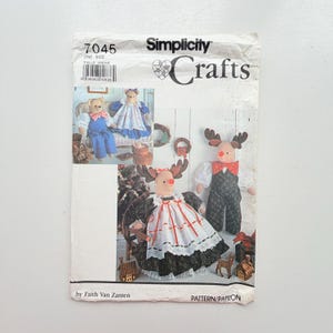 May include: A Simplicity Crafts sewing pattern envelope, number 7045, by Faith Van Zanten. The front displays illustrations of stuffed reindeer and bear figures dressed in fabric clothing, including dresses, overalls, and shirts with red noses.