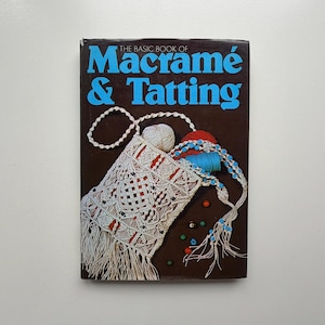 May include: A brown book cover with the title "The Basic Book of Macramé & Tatting" in blue. The cover features a macramé bag with white fringe, yarn, and beads. The bag is white with red accents.