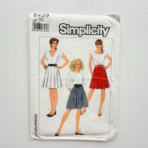 Peut inclure: Une pochette de patron de couture Simplicity, numéro 8439, taille 10. Le devant présente des illustrations de trois tenues : une robe blanche à jupe plissée, un haut blanc avec une jupe à motifs et un haut blanc avec une jupe plissée rouge.