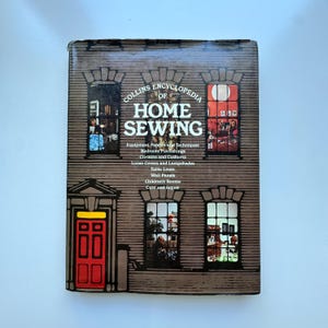 Könnte beinhalten: Ein Vintage-Buch mit dem Titel "Collins Encyclopedia of Home Sewing". Das Cover zeigt eine braune Illustration eines Gebäudes mit Fenstern und einer roten Tür. Der Titel des Buches ist in großen, fetten Buchstaben gehalten.