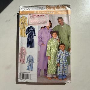 May include: Simplicity pattern 1562A for bathrobes. The pattern shows illustrations of various bathrobe styles in different colours, including yellow, navy, pink, and blue. The package also shows a family wearing the finished robes. The text "@Home easy-to-sew" is visible.