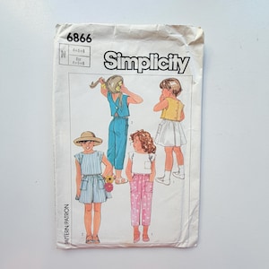 May include: A Simplicity 6866 sewing pattern envelope featuring illustrations of children wearing various outfits including a blue jumpsuit, a yellow top with a white skirt, a blue and white striped dress, and a white top with pink patterned pants.