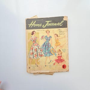 May include: A vintage October 1st, 1958 Australian Home Journal magazine cover featuring illustrations of three figures in floral dresses and a play suit. The cover includes the text These Patterns Enclosed and Two-Way Play Suit 9920.