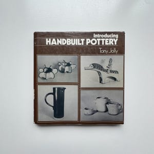 May include: A book cover titled "Introducing Handbuilt Pottery" by Tony Jolly. The cover features four images of pottery, including a pitcher, cups, and decorative pieces. The book is brown with white text and images.