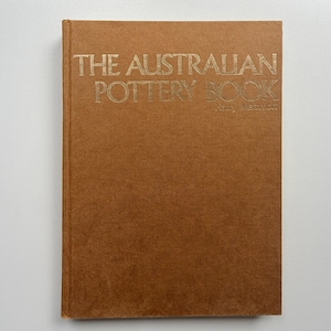 May include: A brown hardcover book with the gold title "THE AUSTRALIAN POTTERY BOOK" and the author's name, Harry Memmott. The book's cover has a textured finish.