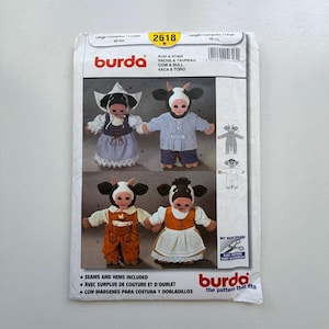 May include: A Burda sewing pattern packet showing cow and bull doll designs. The packet features images of the finished dolls in different outfits, with text in multiple languages. The packet is white with red and black text.