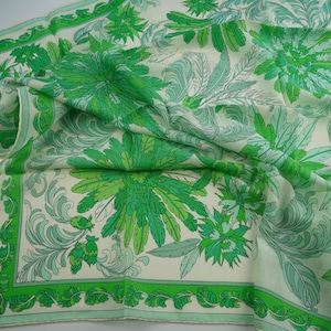 May include: A square scarf featuring a cream-colored background with a repeating pattern of large, vibrant green and light green floral motifs and intricate leafy scrollwork, finished with a solid green border along the outer edges.