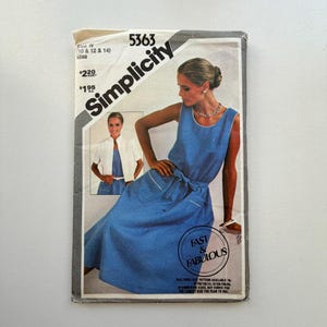 Pode incluir: Padrão de costura Simplicity vintage, tamanho N, apresentando um vestido azul com detalhes brancos e um casaco a condizer. A capa inclui o texto "Simplicity" e "Fast & Fabulous", juntamente com uma foto de uma mulher usando o vestido.
