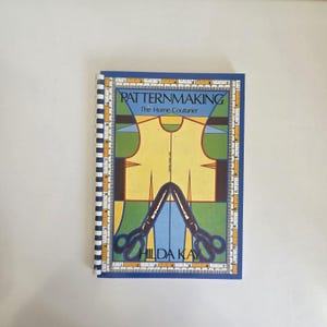 May include: A spiral-bound instructional book titled Patternmaking The Home Couturier by Hilda Kay. The cover features a yellow bodice pattern graphic, blue and green geometric shapes, and a border design resembling a yellow measuring tape.