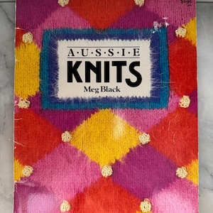 May include: Book cover for "Aussie Knits" with a vibrant diamond pattern in pink, red, yellow, and purple. The title "Aussie Knits" is in bold black letters, with the author's name, Meg Black, below. The cover has a price tag of £2.95.