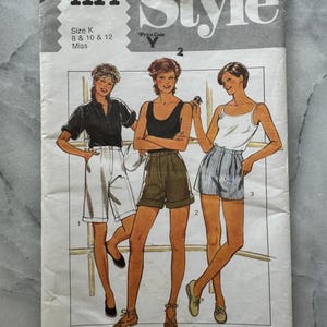 Könnte beinhalten: Vintage Schnittmuster mit dem Titel "Style" mit Illustrationen von drei Frauen in Shorts und Oberteilen. Das Muster enthält die Größen 8, 10 und 12. Das Cover hat die Nummer 4114 und den Text "Pattern/Patron".