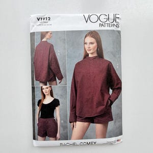 Op de afbeelding: Een Vogue Patterns naaipatroon envelop V1912 met een bordeauxrode top met lange mouwen en opstaande kraag en bijpassende shorts. De verpakking toont drie afbeeldingen van de kledingstukken, de ontwerpersnaam Rachel Comey en maat 18-20-22-24-26.