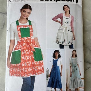 May include: Simplicity sewing pattern S9435 featuring aprons. The pattern includes multiple apron designs, with variations in style and detailing. The aprons are shown in red, green, white, and blue. The pattern size ranges from XS to XL.