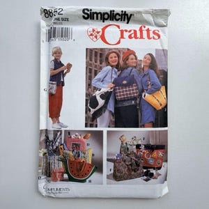 Könnte beinhalten: Simplicity Crafts Schnittmusterumschlag mit verschiedenen Taschenentwürfen. Der Umschlag enthält Bilder von Tragetaschen, Picknickkörben und Handtaschen. Der Text auf dem Umschlag lautet "Simplicity Crafts" und "ONE SIZE".