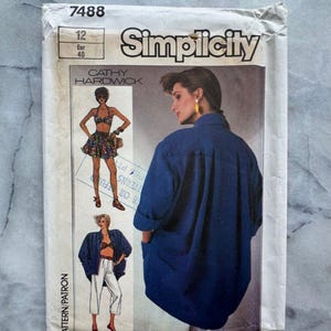 Può includere: Un modello di cucito Simplicity vintage con un design di camicia blu. Il pacchetto del modello include illustrazioni dei capi finiti e il testo "Simplicity", "Cathy Hardwick" e le informazioni sulle taglie.