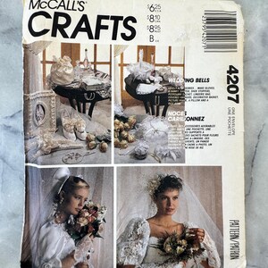 May include: A McCall's Crafts sewing pattern envelope 4207 for wedding accessories. The front features images of gloves, a garter, a lingerie bag, a basket, a picture frame, a pillow, and a rose, with two models wearing veils and lace.