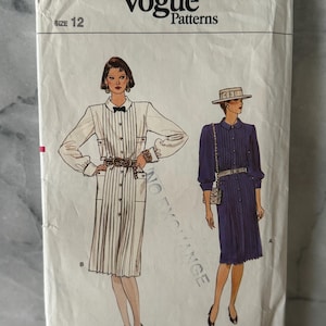 May include: Vintage Vogue Patterns envelope with illustrations of two dresses. The envelope is off-white and features the text "Vogue Patterns" and "Size 12". One dress is white with vertical pleats, the other is a dark blue, button-down dress.