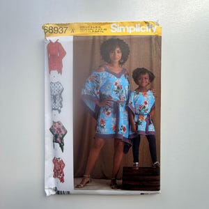 Op de afbeelding: Simplicity naaipatroon 68937 A. De afbeelding toont een vrouw en kind in bijpassende blauwe bloemenjurken met paarse afwerking. Het patroon bevat illustraties van verschillende jurkstijlen. De maat is S-XL.