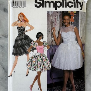 Pode incluir: Padrão de costura Simplicity 7824, com ilustrações de três vestidos formais. O padrão inclui tamanhos N (10-14). Os vestidos incluem um vestido preto sem alças, um vestido rosa e floral e um vestido branco com um laço.
