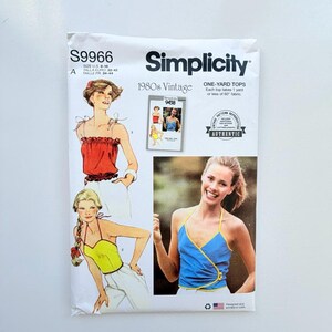 May include: A Simplicity S9966 sewing pattern envelope for 1980s vintage one-yard tops. The white paper packaging features illustrations of two different top styles in red and yellow, and a photograph of a blue wrap-style top with yellow trim.