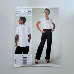 Op de afbeelding: Een naaipatroon van Anne Klein New York. Het patroon toont een damesoutfit met een witte top met korte mouwen en een zwarte broek. Het patroonnummer is V1294. Het logo Vogue Patterns American Designer is zichtbaar.