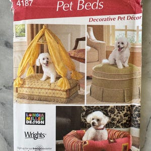May include: A Simplicity Home Decorating pattern for Pet Beds. The cover features images of decorative pet beds, including a canopy bed, a round bed, and a cushioned ottoman. The pattern includes the text "Decorative Pet Décor".