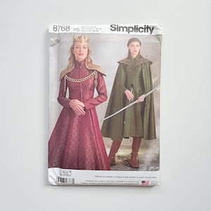 Könnte beinhalten: Ein Simplicity 8768 Schnittmusterumschlag mit zwei Kostümdesigns. Eines ist ein rotes Kleid mit langen Ärmeln, Goldkettendetail und Krone. Das andere ist ein grünes Kleid mit Umhang und Schwert. Der Text enthält die Größe H5 und die Nummer 8768.
