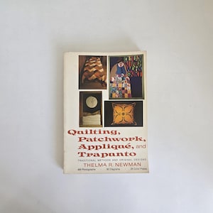 Peut inclure: Un livre à couverture souple intitulé Quilting, Patchwork, Appliqué, and Trapunto par Thelma R. Newman. La couverture blanche présente quatre encarts photographiques montrant divers projets textiles, avec du texte rouge détaillant 400 photographies, 30 diagrammes et 26 planches en couleur.