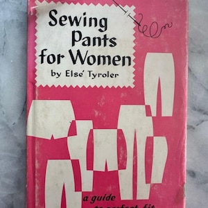 Könnte beinhalten: Ein Vintage-Nähbuch mit dem Titel "Sewing Pants for Women" von Else Tyroler. Das Cover ist rosa mit weißem Text und Illustrationen von Hosenmustern. Eine Nadel- und Faden-Grafik befindet sich in der oberen rechten Ecke. Der Untertitel des Buches lautet "a guide to perfect fit."