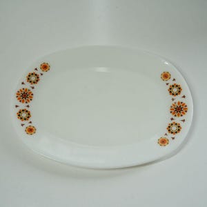 May include: White oval serving platter with a decorative floral pattern in orange, brown, and yellow. The pattern is arranged in a semi-circle on each end of the platter. A vintage piece for serving food.