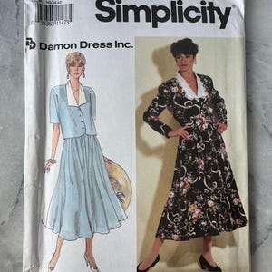 Könnte beinhalten: Simplicity Schnittmuster 7371 mit zwei Kleiderdesigns. Ein Kleid ist ein hellblauer Rock und eine Jacke mit weißem Kragen. Das andere ist ein schwarzes Blumenkleid mit weißem Kragen. Größe H5 (6-14).