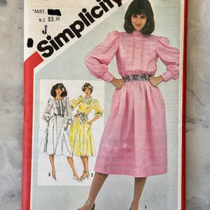 May include: Vintage Simplicity sewing pattern, size 10 Miss. The pattern features a pink dress with long sleeves and a decorative belt. The pattern cover includes illustrations of the dress in different colours and styles.